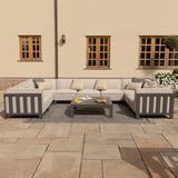 A sectional outdoor sofa and coffee table set on a patio, with cushions and decorative pillows, near a building with wooden windows and a lantern.