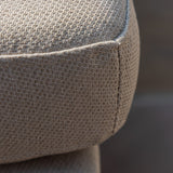 A close-up of a textured fabric, possibly on furniture, with tight, intricate weaving and a curved edge, against an indistinct, soft-focus background.