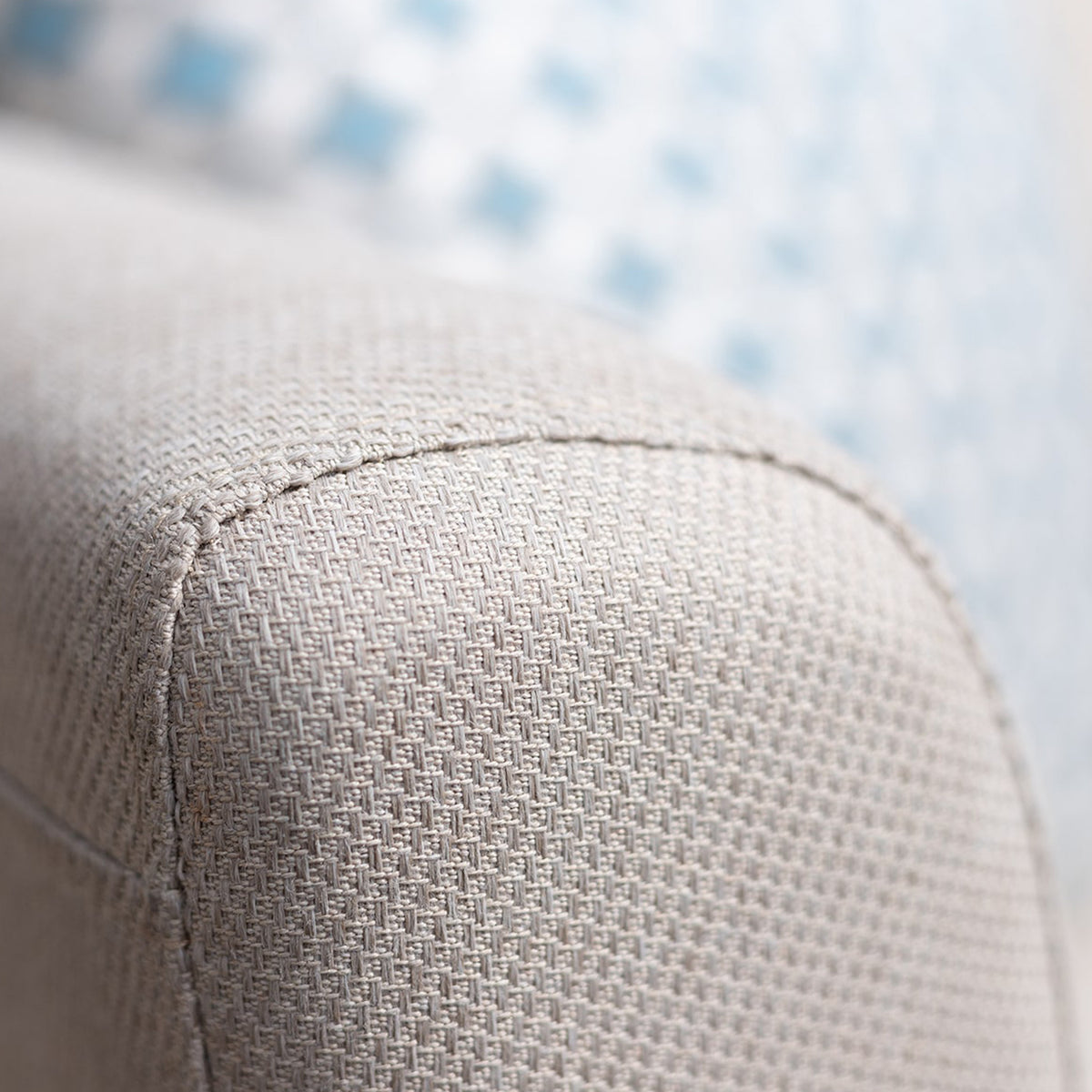 A close-up of a sofa's textured upholstery with the edge of a blue cushion in the blurry background.
