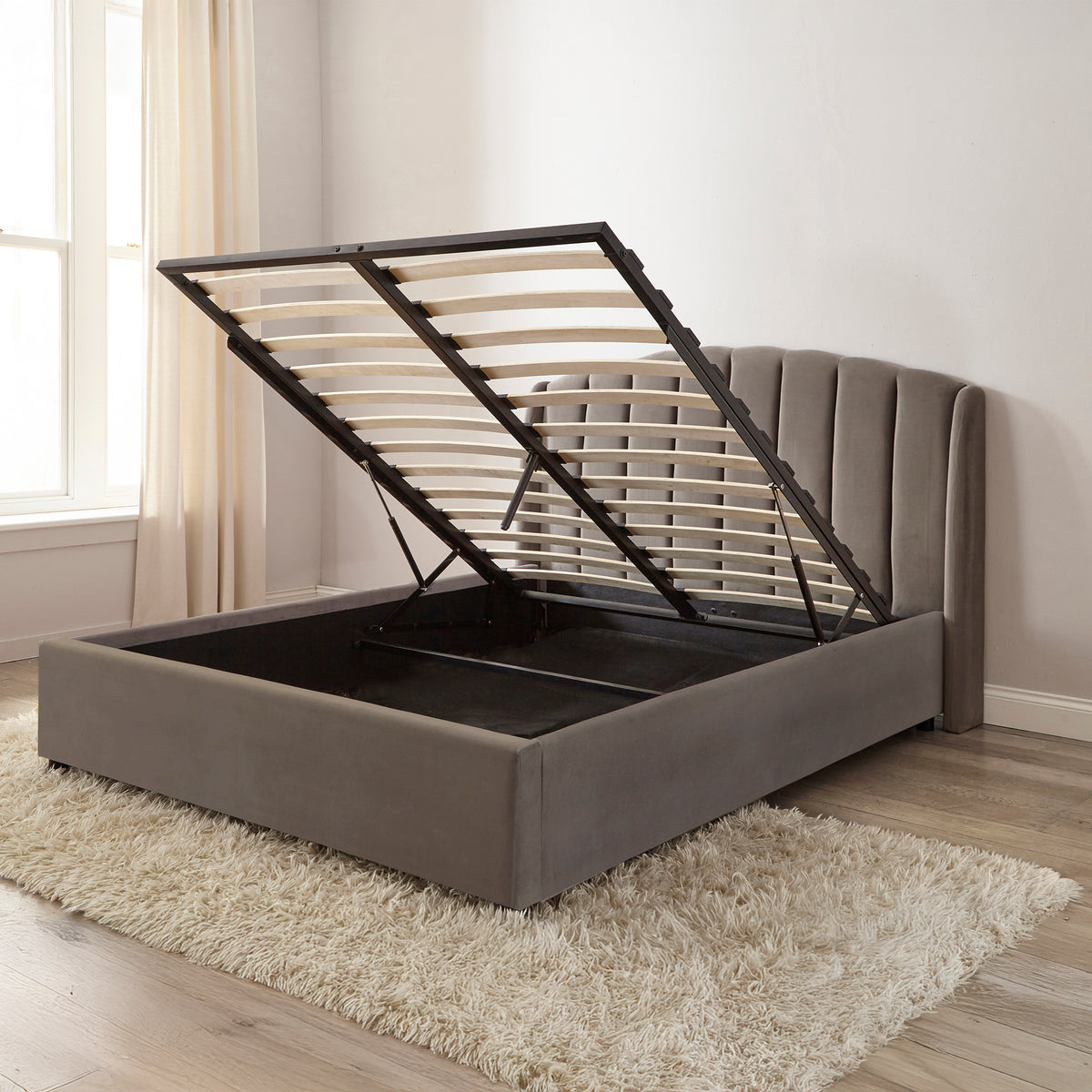 Gray upholstered bed with storage compartment in a room with a window and rug.