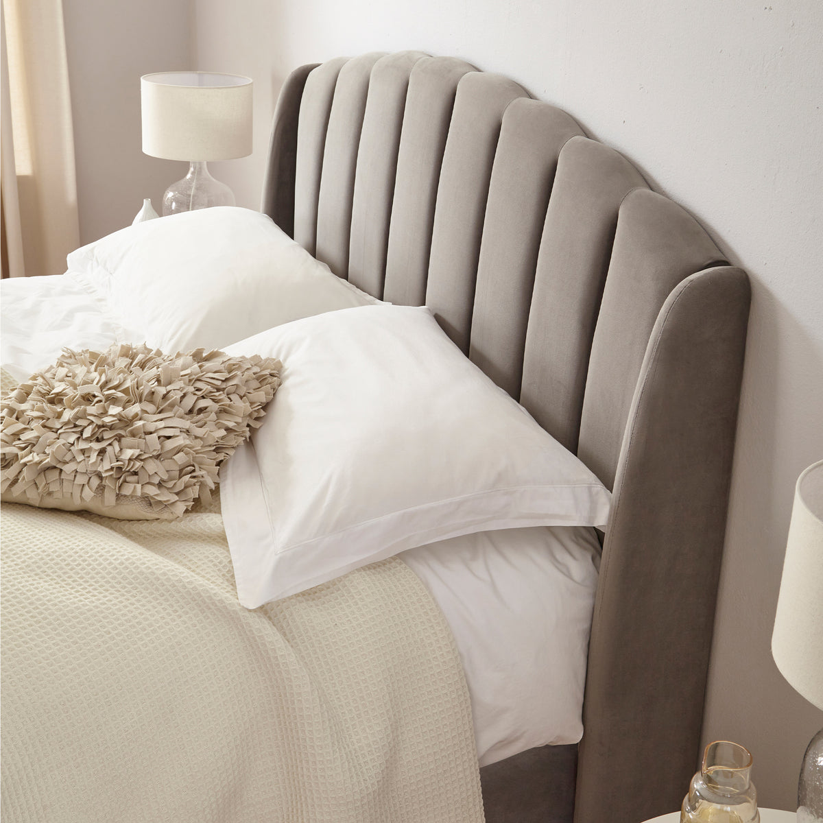 Gray upholstered headboard with pillows and a blanket in a bedroom setting.