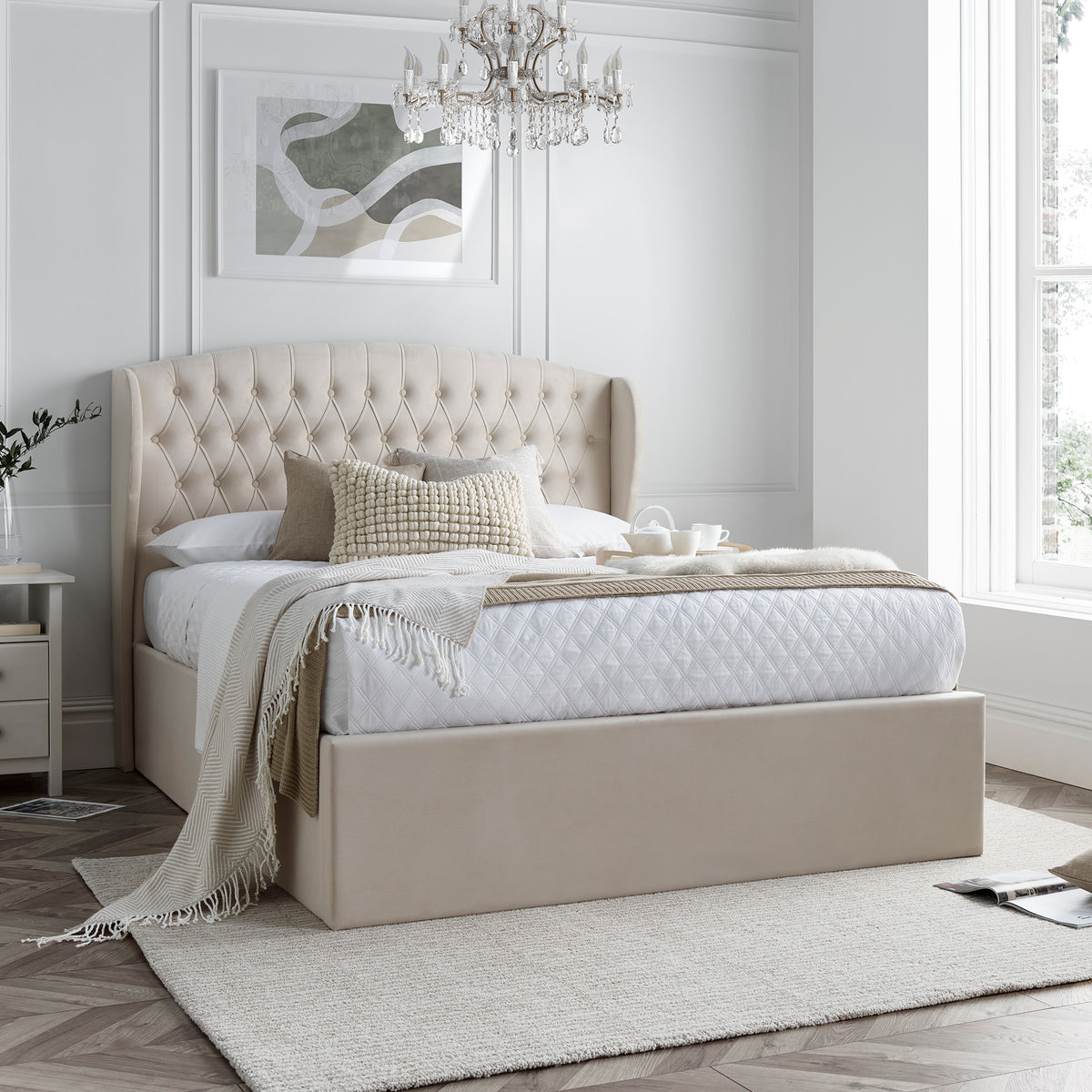 A natural upholstered bed with a tall, tufted headboard is set against a paneled wall on herringbone-patterned wooden flooring.