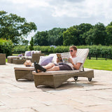 A person reclines on an outdoor sun lounger, reading a magazine titled "COUNTRY HOMES," amidst a patio setting with furniture and lush greenery in the background.