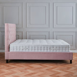 A pink, tufted single bed against a grey paneled wall, on a herringbone patterned wooden floor.