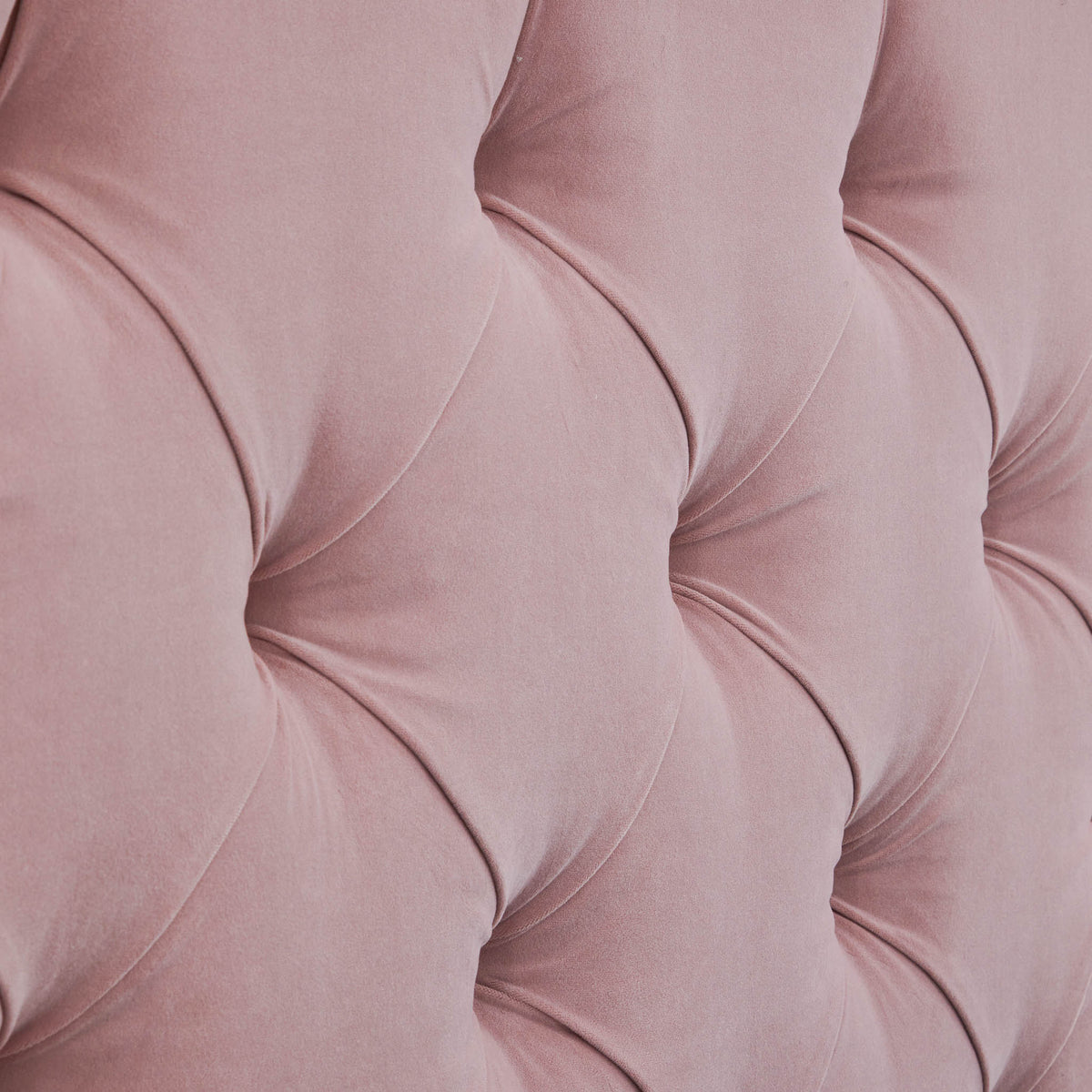 A close-up of a pink, tufted fabric forming a diamond pattern with visible stitching and shadows accentuating its plush texture.