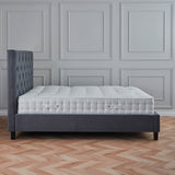 A single gray upholstered bed with a quilted mattress is centered against a wall with decorative panels, placed on a herringbone patterned wooden floor.