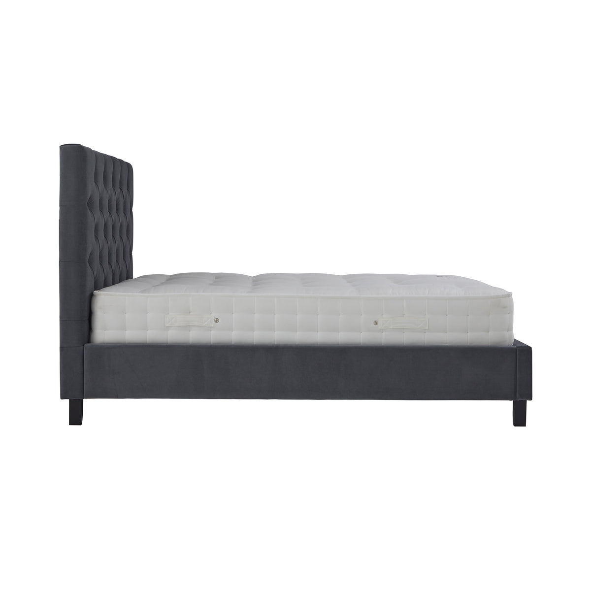 A dark gray upholstered bed frame with a tall, tufted headboard holds a thick white mattress in an evenly lit, blank setting.