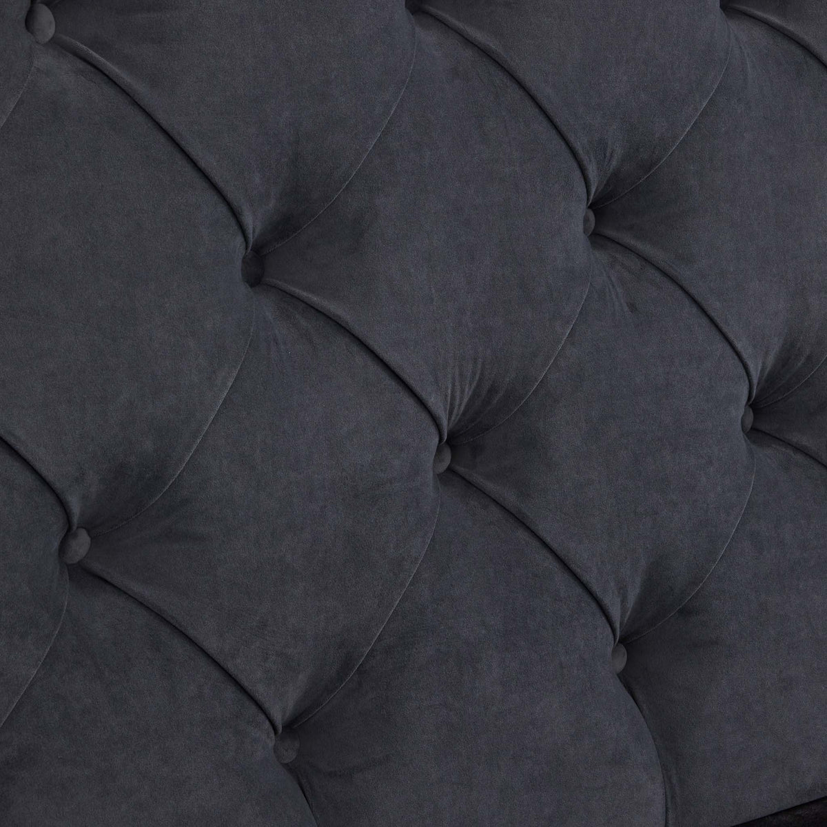 A close-up of a grey, tufted fabric surface with buttons creates a diamond pattern, likely part of a cushioned furniture piece.