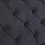 A close-up of a grey, tufted fabric surface with buttons creates a diamond pattern, likely part of a cushioned furniture piece.