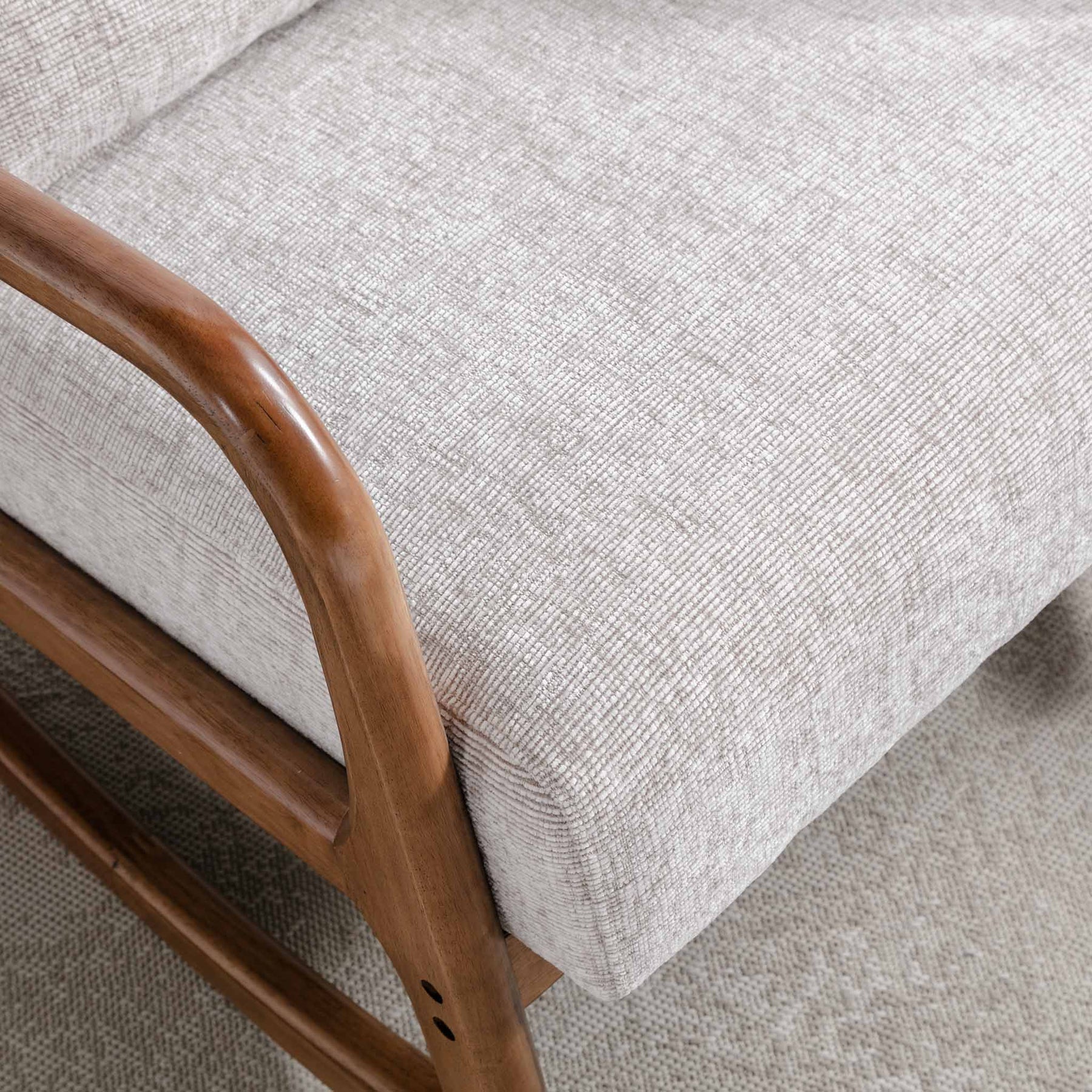 A close-up of a textured, beige upholstery on a cushioned chair with a smooth, wooden armrest. The context is nondescript with a focus on detailing and materials.