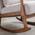 A close-up of a wooden rocking chair's armrest and base, highlighted by textured upholstery, resting on a smooth carpet.