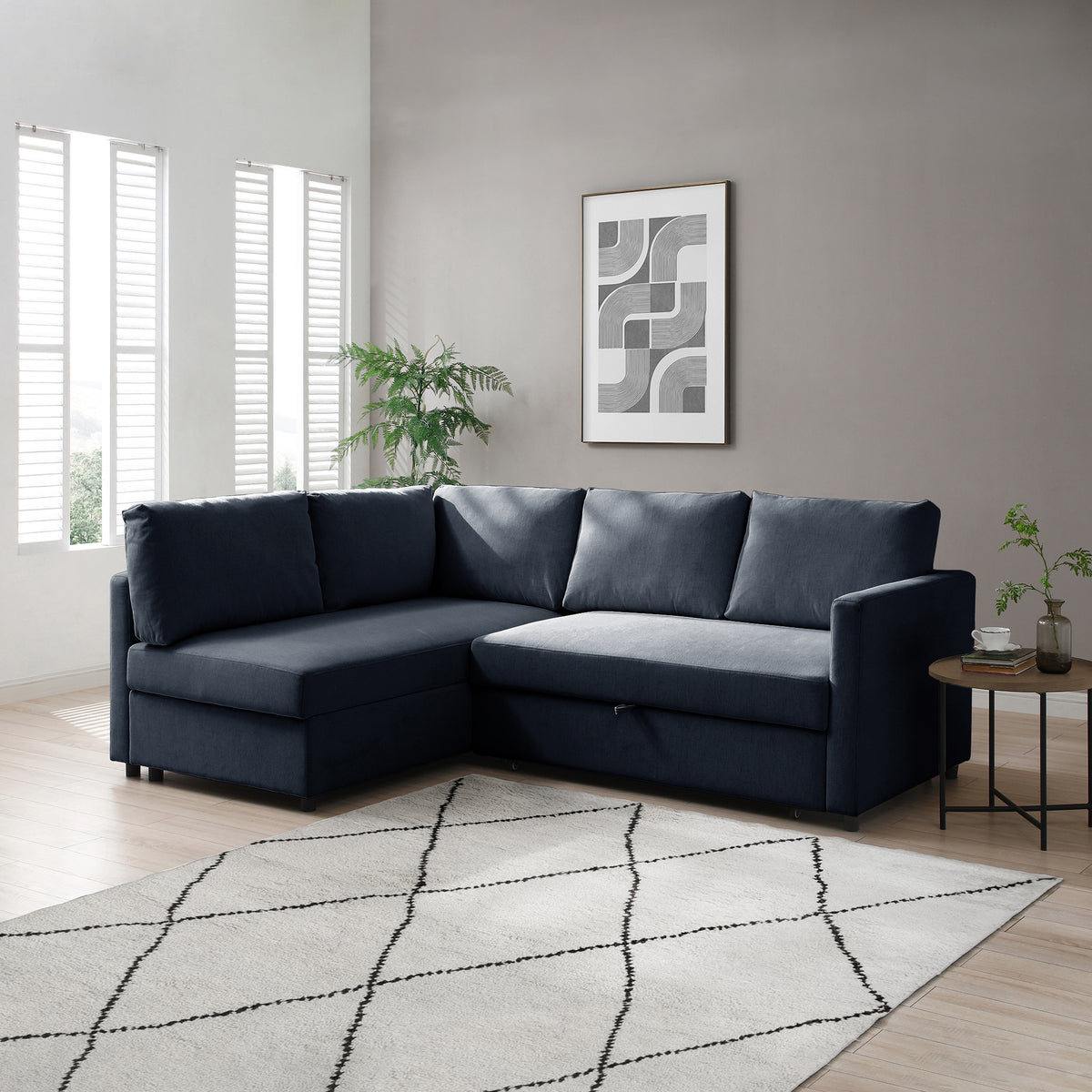 A navy blue sectional sofa rests in a minimalist living room adorned with a geometric-patterned rug, abstract art, and small green plants.