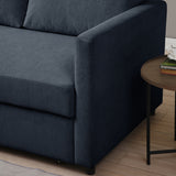 A navy blue sofa with a smooth texture, adjacent to a round wooden side table with books, placed in a room with wooden flooring.