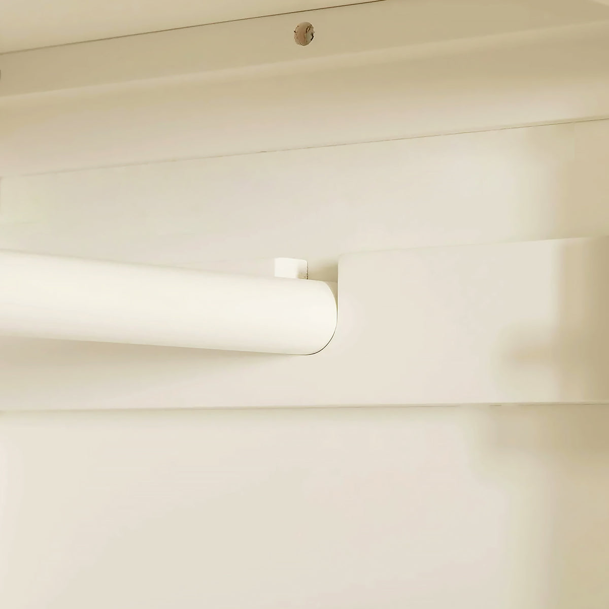 A white roller blind is partially rolled up against a beige wall, near a ceiling with a visible screw.