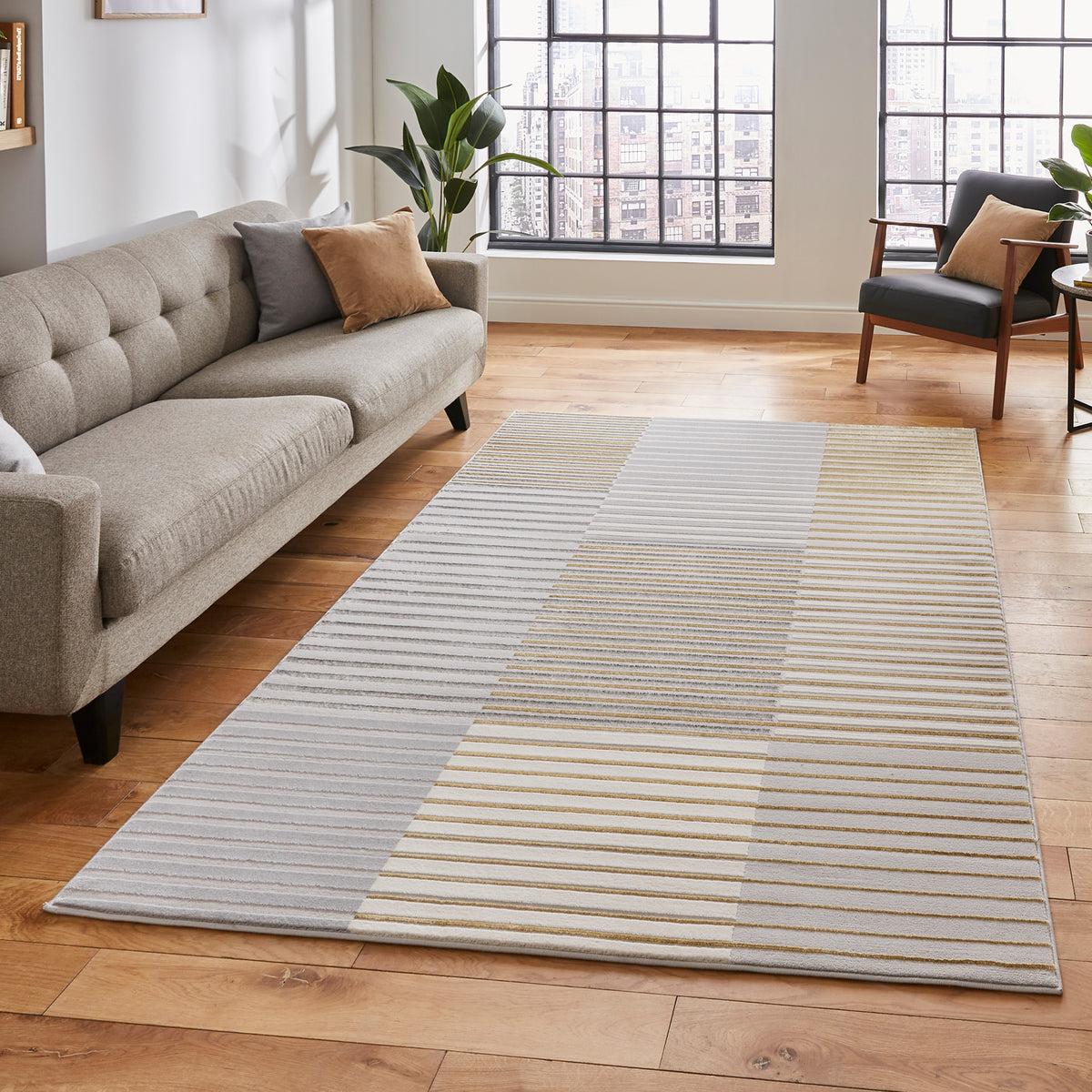 A striped area rug lies on a wooden floor, flanked by a grey sofa and a black armchair, with large windows revealing a cityscape.