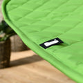 A close-up of a bright green, quilted fabric with a black label featuring a white design, possibly indicating a brand, placed on a blurry indoor background.