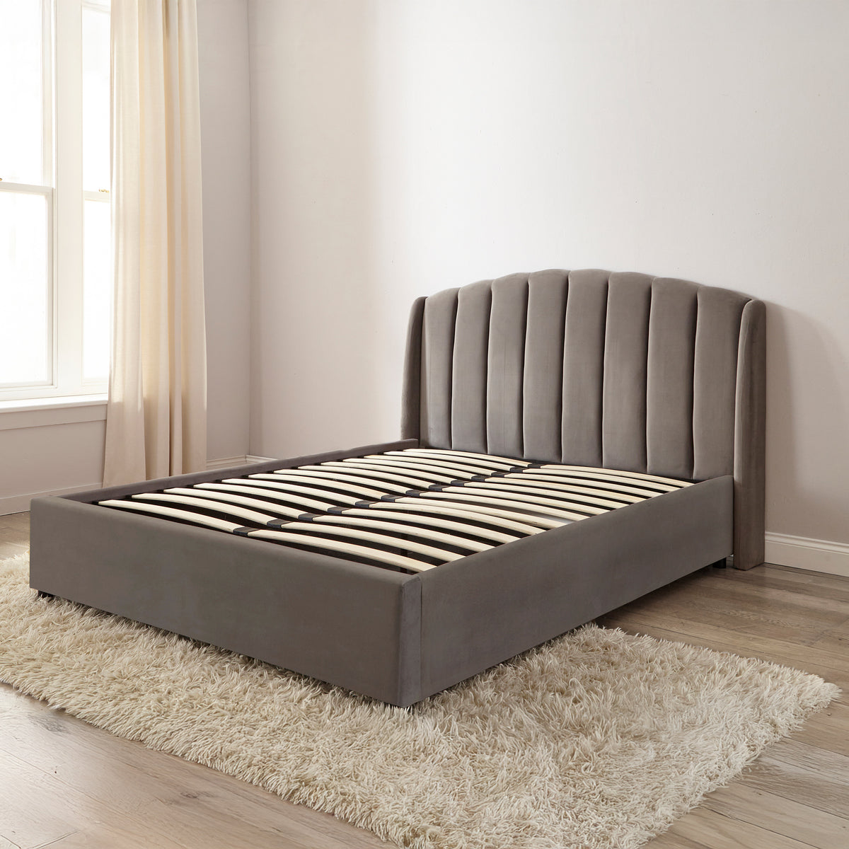 Gray upholstered bed in a room with a window and beige curtains.
