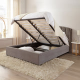 Gray upholstered bed with open storage compartments in a room with a window and side table.