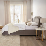 Neatly made bed with gray headboard in a bright bedroom