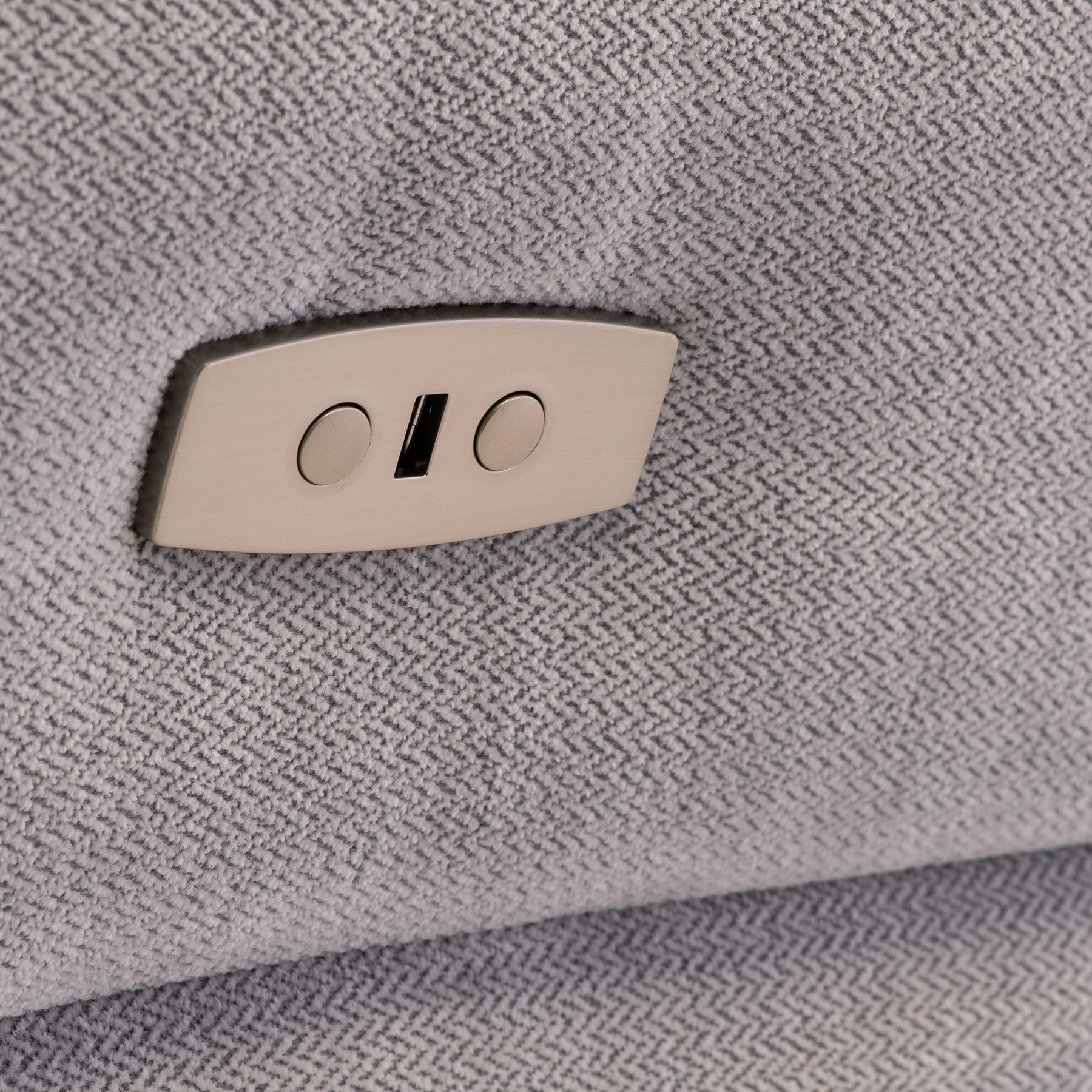 A beige recliner lever on a textured gray fabric. The lever appears flush against the upholstery, suggesting an adjustable furniture feature.