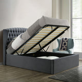 A gray upholstered bed with a lifted mattress reveals storage underneath, positioned against a paneled wall on a herringbone wood floor.