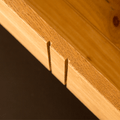 Wooden dovetail joints protrude from a panel, demonstrating craftsmanship against a dark background.