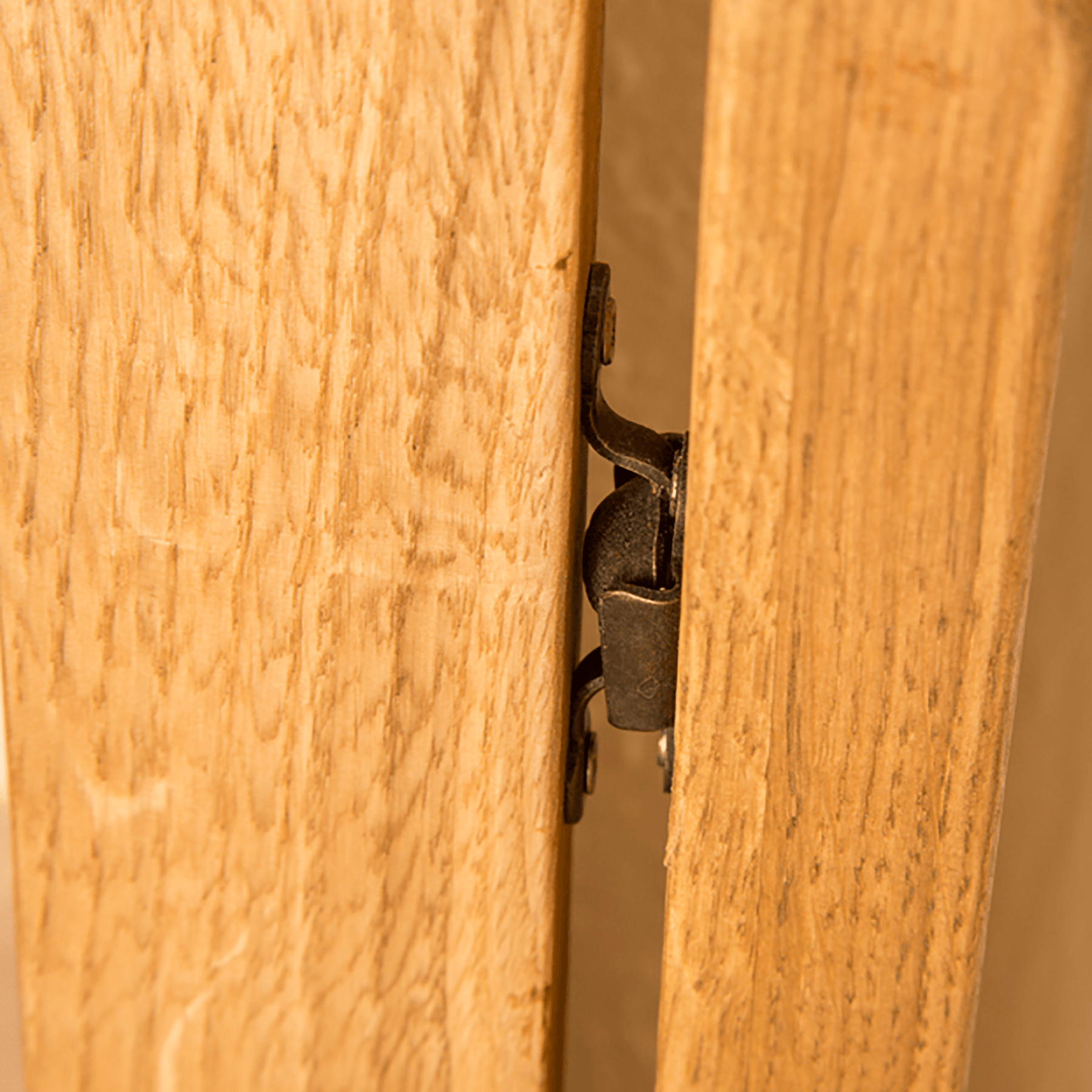 Metal hinge connecting two wooden panels, partially concealed between them, suggesting a door or cabinet in a wooden structure.