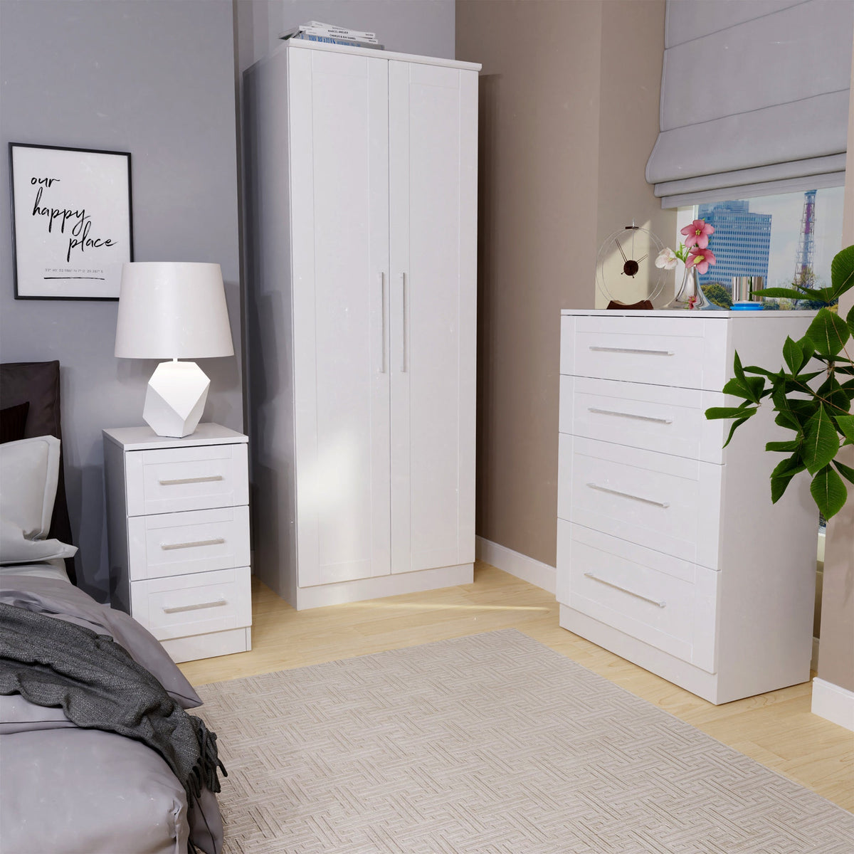 White bedroom furniture sits in a tidy room, with a wardrobe, a chest of drawers, and a nightstand. A framed quote reads "our happy place" on the wall.