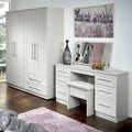 A white wardrobe and a matching vanity table with a stool are arranged in a room with wooden flooring and decorative elements, creating a contemporary bedroom setting.
