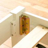 A metal hinge connects two white wooden structures, enabling pivoting motion, set against a wooden floor background.