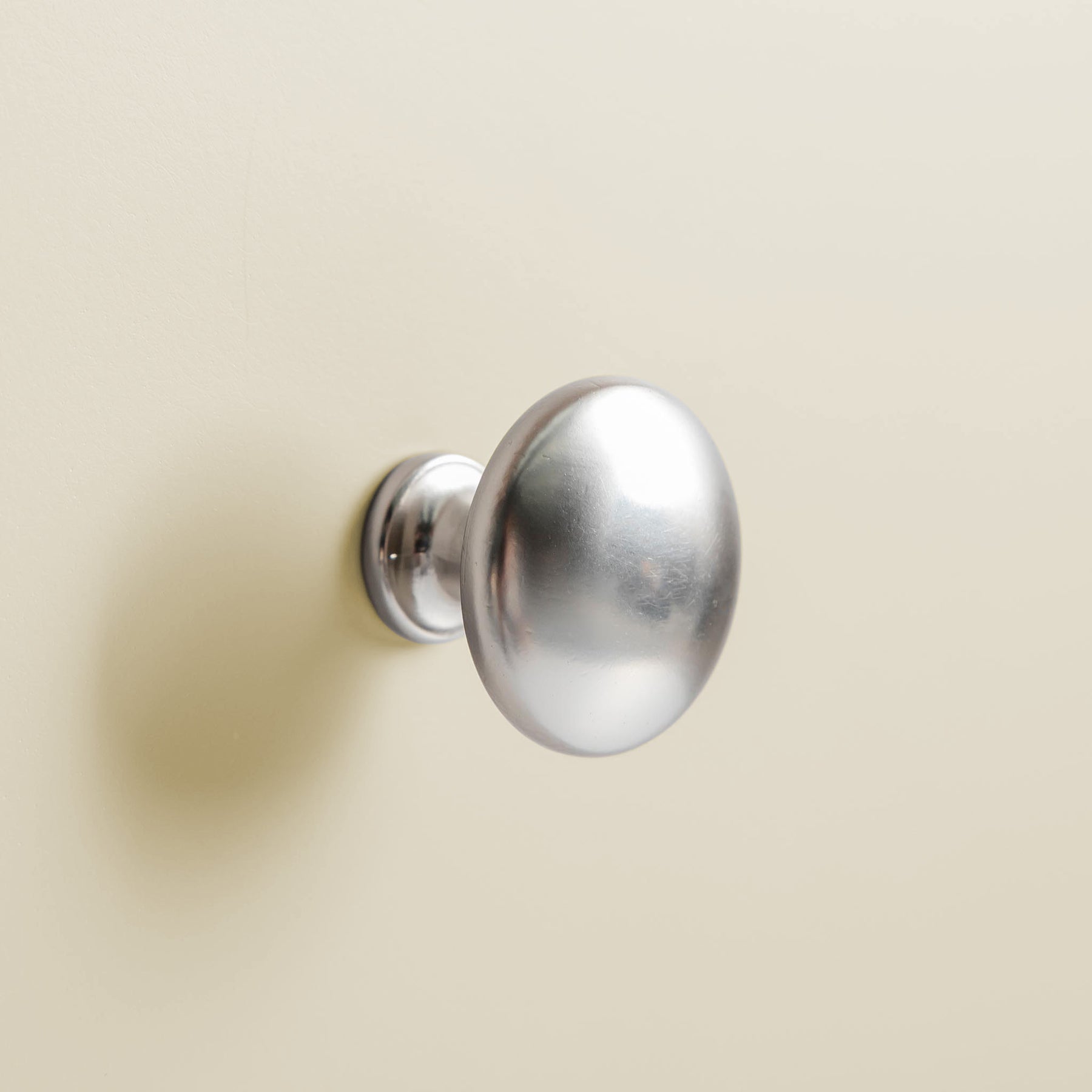 A round, metallic doorknob is mounted on a beige wall, reflecting soft light.