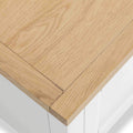 A close-up of a light wooden tabletop corner, showcasing its texture and the precision of its right-angled joint, all against a blurred white background.