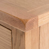 A close-up of a wooden table corner showing the texture and grain, with a blurred background emphasizing the woodworking detail.
