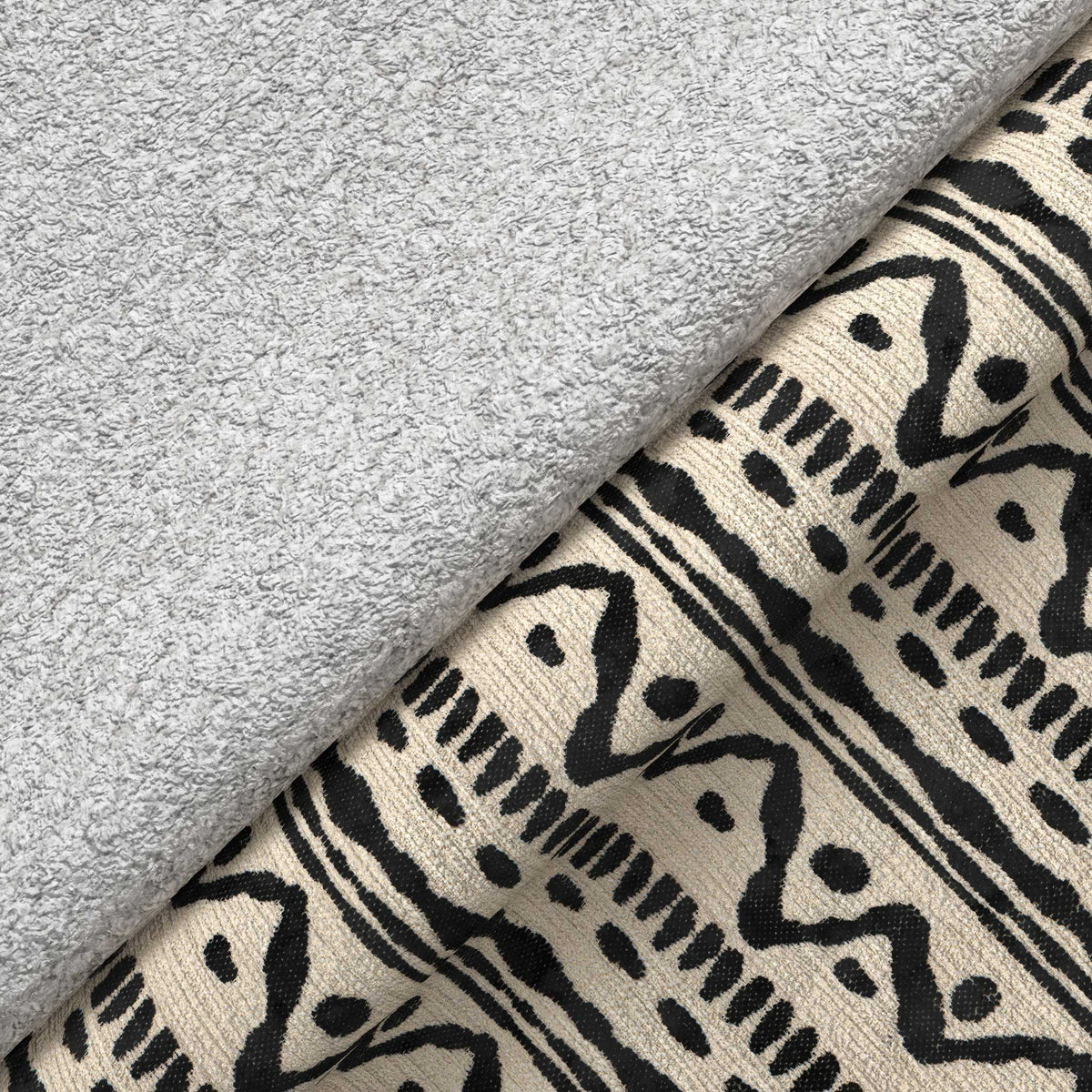 A rolled-up gray towel rests on a patterned beige fabric with black geometric designs, depicting a simple, textured domestic scene.