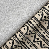 A rolled-up gray towel rests on a patterned beige fabric with black geometric designs, depicting a simple, textured domestic scene.