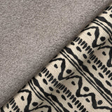 A grey fluffy towel overlaps a patterned fabric with geometric black designs on a beige background, suggesting a home decor setting.