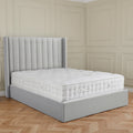 A grey upholstered bed with a plush mattress in an elegant room with paneled walls and herringbone wood flooring.