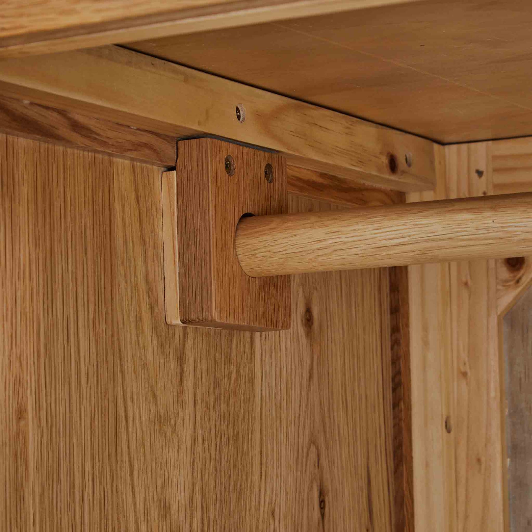 A wooden dowel passes through a bracket, securing it against a vertical wooden surface, likely part of a furniture assembly.