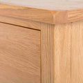 A close-up of a wooden piece, featuring the corner of a light oak tabletop above a vertical grain panel, showcasing woodworking craftsmanship and material texture.