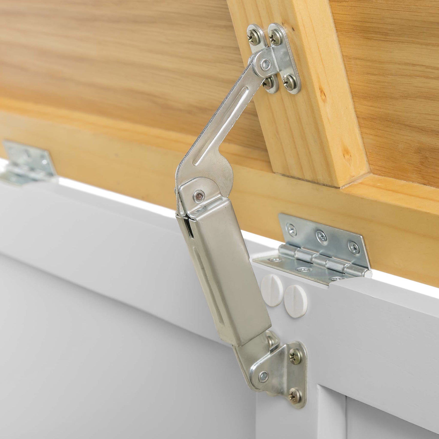 A silver hydraulic cabinet hinge connects a wooden cabinet door to a white structure, demonstrating its function and installation.