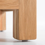 A wooden table leg with a small protective pad stands on a white surface, showcasing the texture and joinery detail.