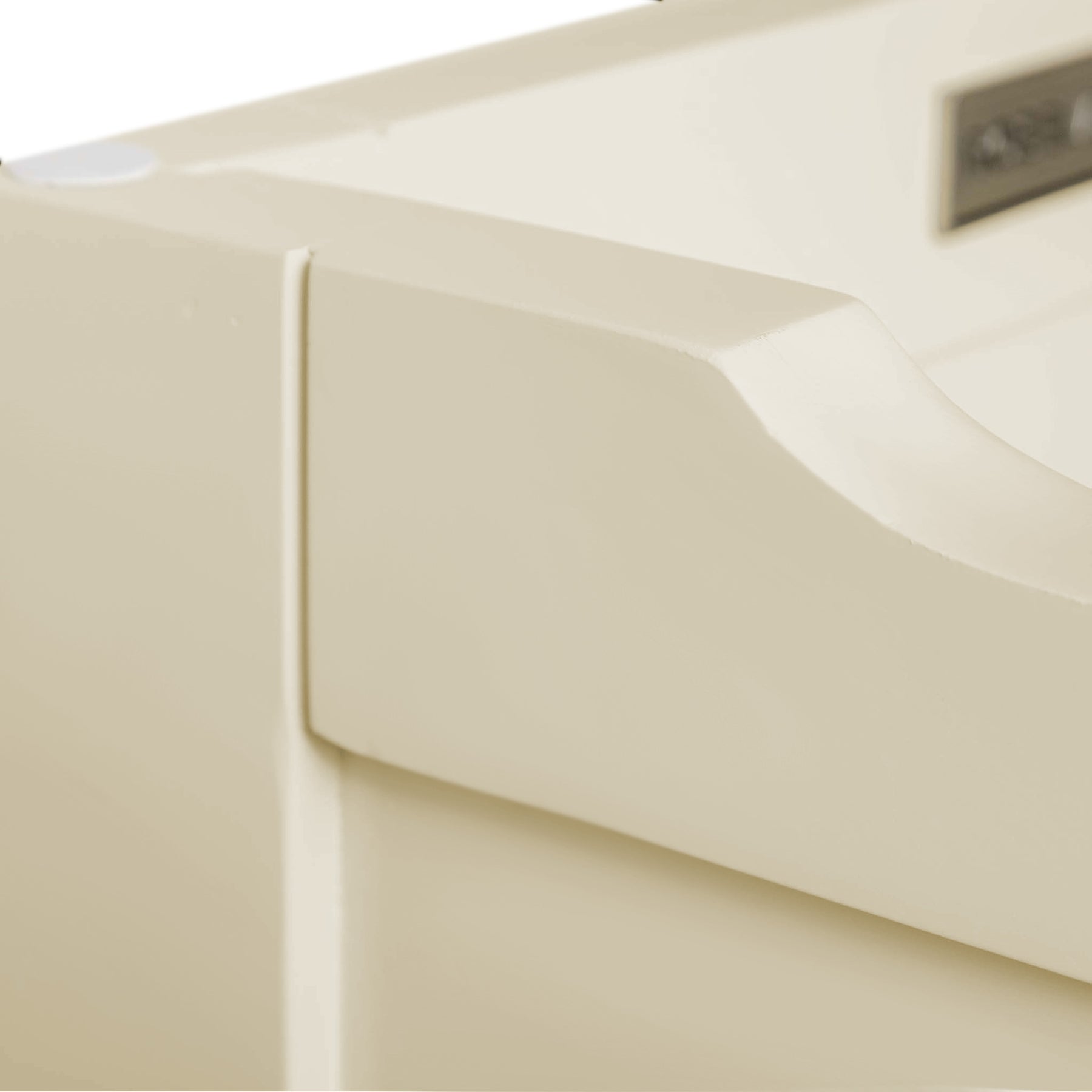 A close-up of a beige object with smooth curves and a rectangular label or emblem, possibly a part of plastic machinery or equipment, against a neutral background.