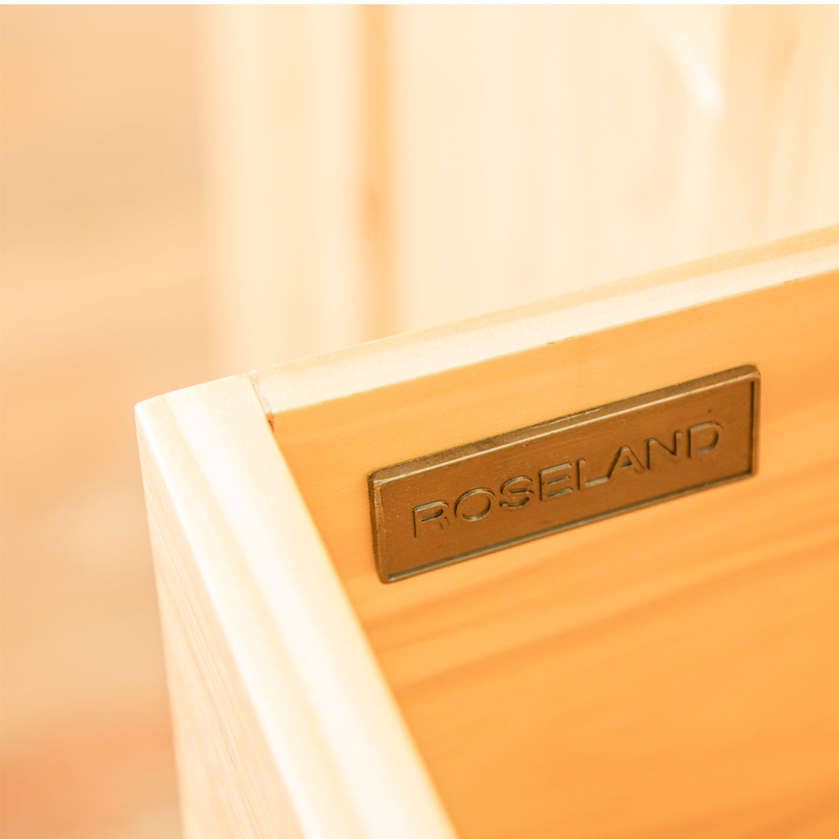 A bronze plaque engraved with "ROSELAND" is affixed to a pale wooden surface, possibly furniture, with a soft-focus background.
