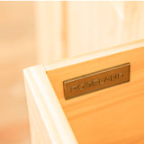 A bronze plaque engraved with "ROSELAND" is affixed to a pale wooden surface, possibly furniture, with a soft-focus background.