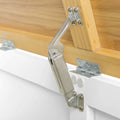 A silver gas spring door lift mechanism connects a wooden cabinet to its white door, holding it open against a plain background.