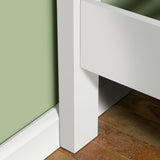 A white, rectangular structure intersects a green wall above a white baseboard, set against a terracotta-tiled floor—implying a minimalist, modern interior corner.
