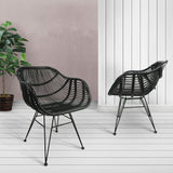 Two black modern chairs with thin, curved lines are placed on a white wooden floor, contrasting with a white vertical-striped wall and a pink wall with a green potted plant.