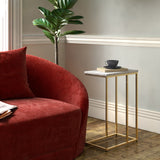 A red curved sofa next to a slender gold side table with a cup and books, in a room with a potted plant and classic molding.