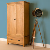 A wooden armoire stands next to a tripod-based spotlight lamp against a teal wall on a beige carpet.