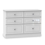 A white six-drawer dresser with silver knobs stands stationary against an isolated white background.